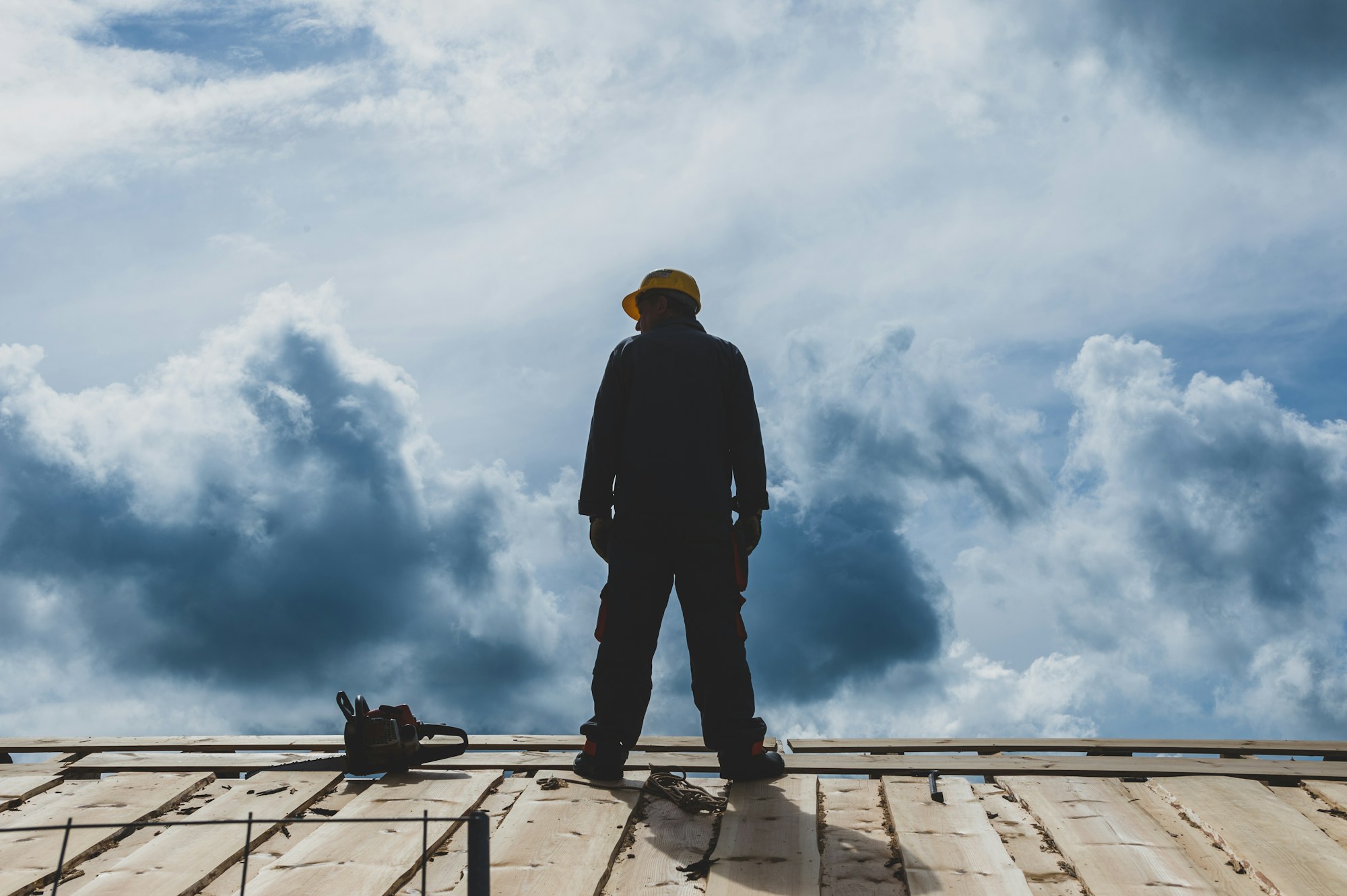 Dachdecker mit Helm steht auf einem Dach vor dramatischem Wolkenhimmel
